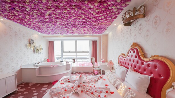 Une chambre à coucher luxueuse avec un grand lit, une tête de lit rose et un plafond recouvert de fleurs.