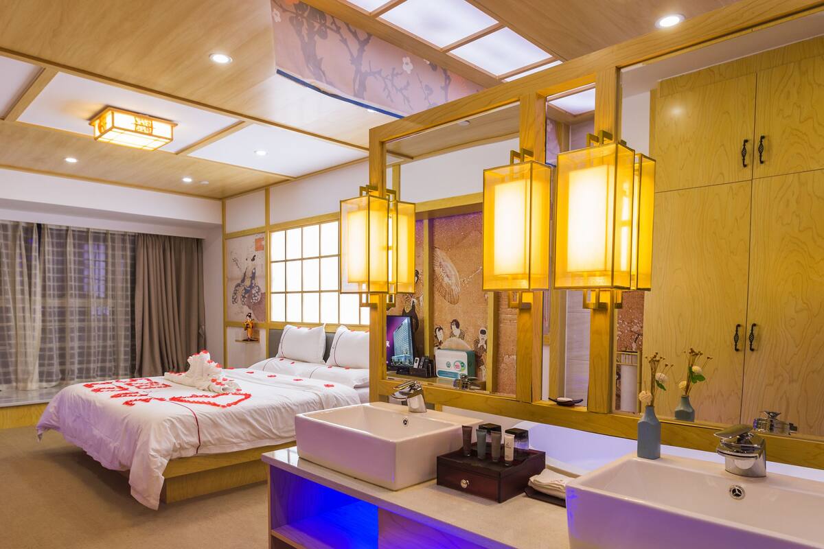 A hotel room with a large bed, a double sink vanity, and a large mirror.