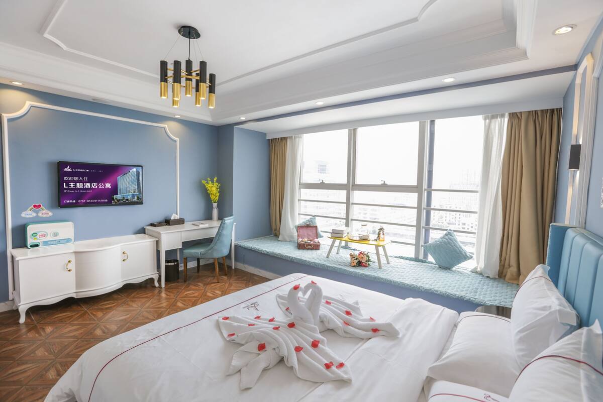 A hotel room with a bed, a desk, a television, a window with curtains, and a view of the city.