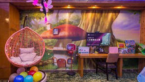 Une pièce décorée d’une fresque représentant une cabane dans un arbre, avec un fauteuil suspendu, un bureau doté d’un ordinateur et des ballons de couleurs vives.
