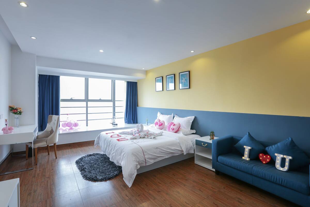 A modern bedroom with a bed, a desk, a sofa, and a window with curtains.