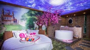 Une chambre à coucher avec un grand lit, une fresque murale représentant un ciel étoilé, un arbre, et une salle de bain avec une baignoire et un lavabo.