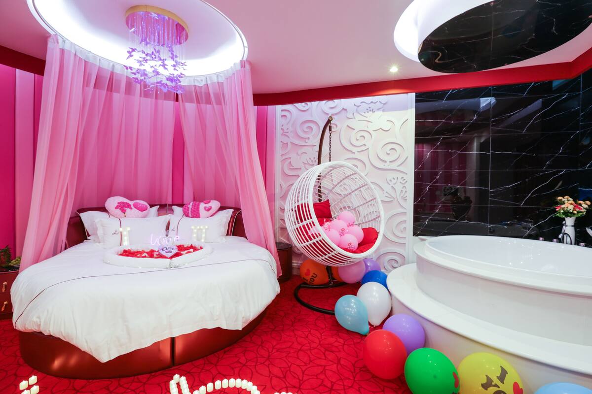 A luxurious bedroom with a large bed, a white canopy, a white hanging chair, and a bathtub.