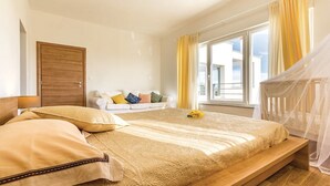 A bedroom with a bed, a bedside table, a window with curtains, a white sofa with cushions, and a wooden door. - Villa Morning View, sunrise and relax on southernmost point in Istrian peninsula (Ližnjan)