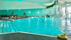 An indoor swimming pool with a slide, a diving platform, and a few people swimming.