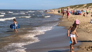 A beach with people walking along the shore, some carrying beach gear.
