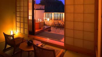 A traditional Japanese room with tatami flooring, a low table, and a sliding door leading to an outdoor deck with a wooden fence and a hot tub.