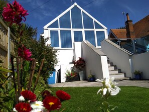 Une maison moderne dotée d’un toit triangulaire imposant, d’un escalier menant à l’entrée et d’une pelouse bien entretenue agrémentée de fleurs.