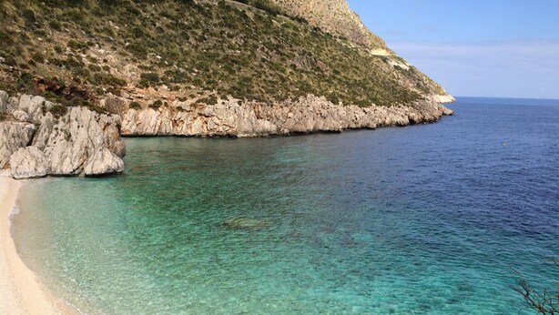 Eine Küstenlandschaft mit klarem türkisblauem Wasser, einem Sandstrand und steinernen Klippen.
