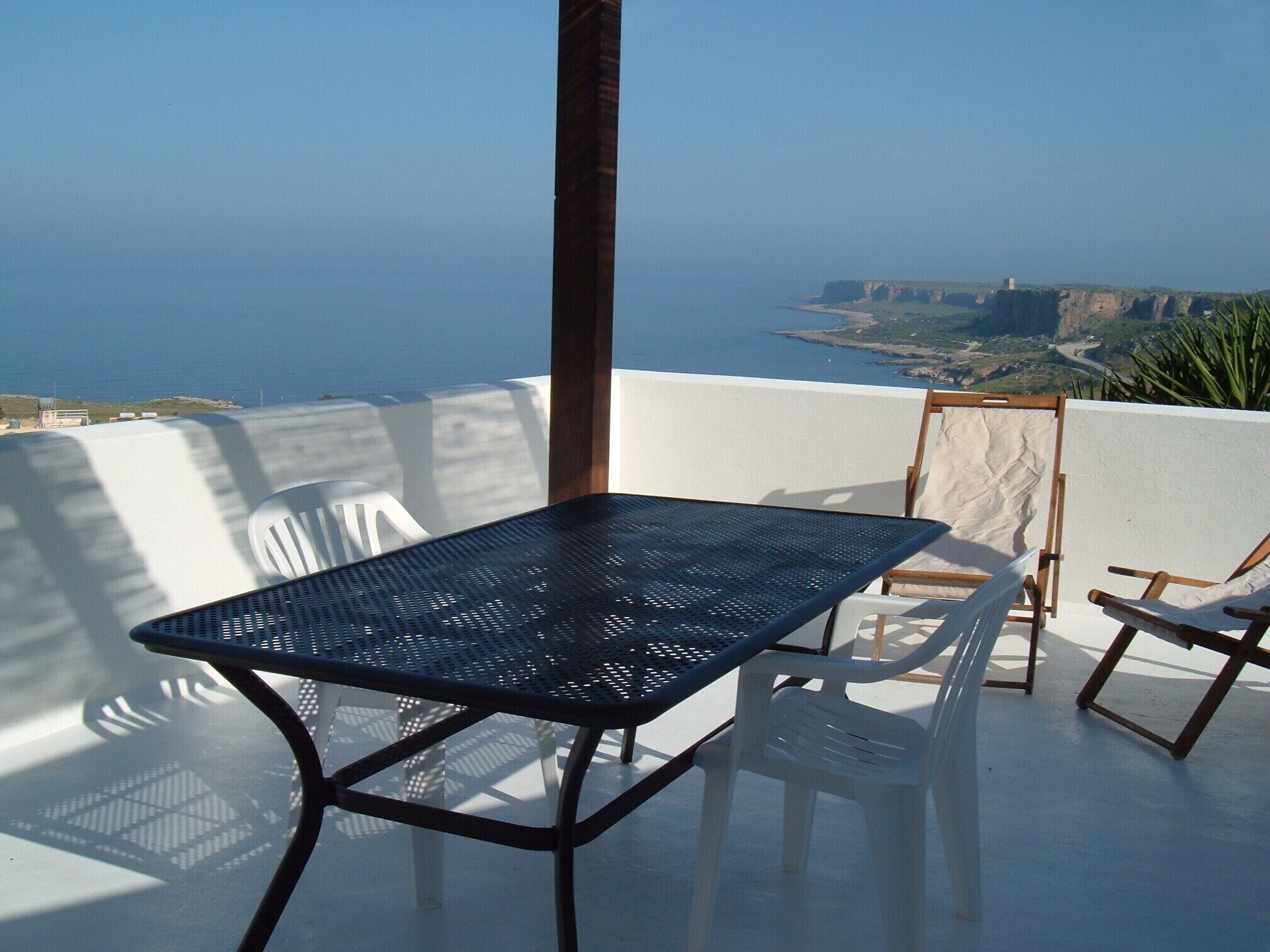 A terrace with a table and chairs, overlooking a coastal landscape.