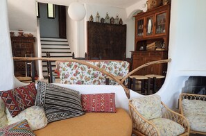 A cozy living room with a sofa, patterned cushions, a wicker chair, and a wooden cabinet with glass doors. - Seafront home, Torre delle Stelle, Sardinia (Torre Delle Stelle (Maracalagonis))