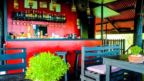Zona de bar con pared roja, sillas de madera y una mesa con planta en maceta.