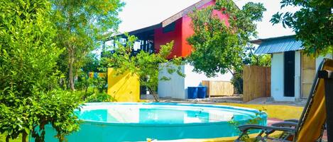 A swimming pool with a yellow deck, surrounded by trees and a red building.