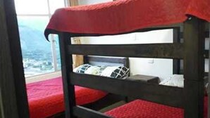 A bunk bed with red bedding in a room with a large window and a painting on the wall.