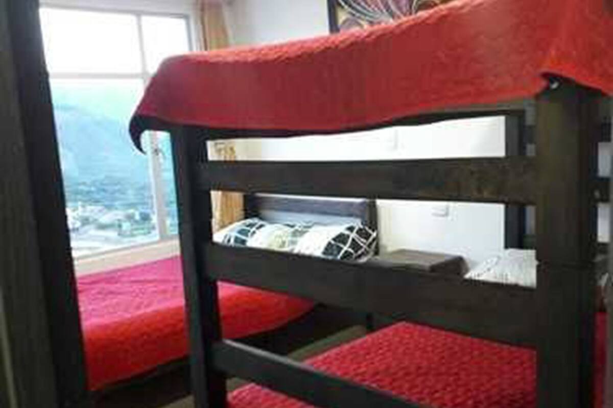 Una litera con ropa de cama roja en una habitación con un ventanal grande y un cuadro en la pared.