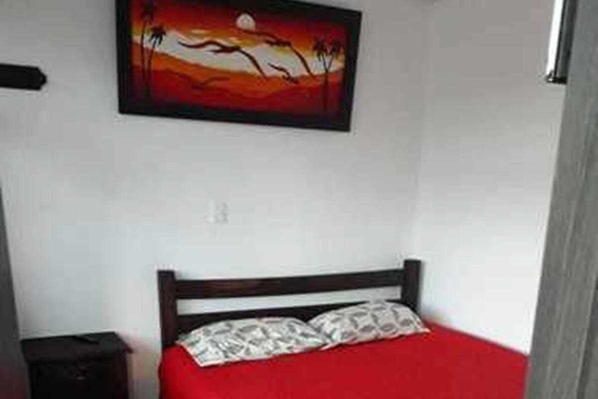 Un dormitorio con cama, mesita de noche, un cuadro en la pared y una puerta.