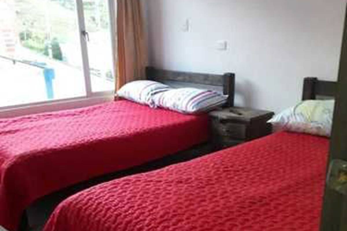 Una habitación con dos camas, cada una con una colcha roja, una mesita de noche y un cuadro colgado en la pared.