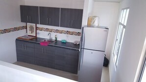A compact kitchen with dark cabinets, a white refrigerator, and a tiled backsplash.