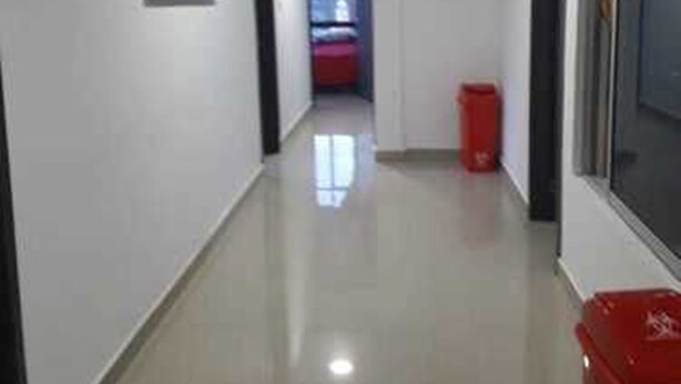 A corridor with a framed picture on the wall, a red trash bin, and a window on the right.