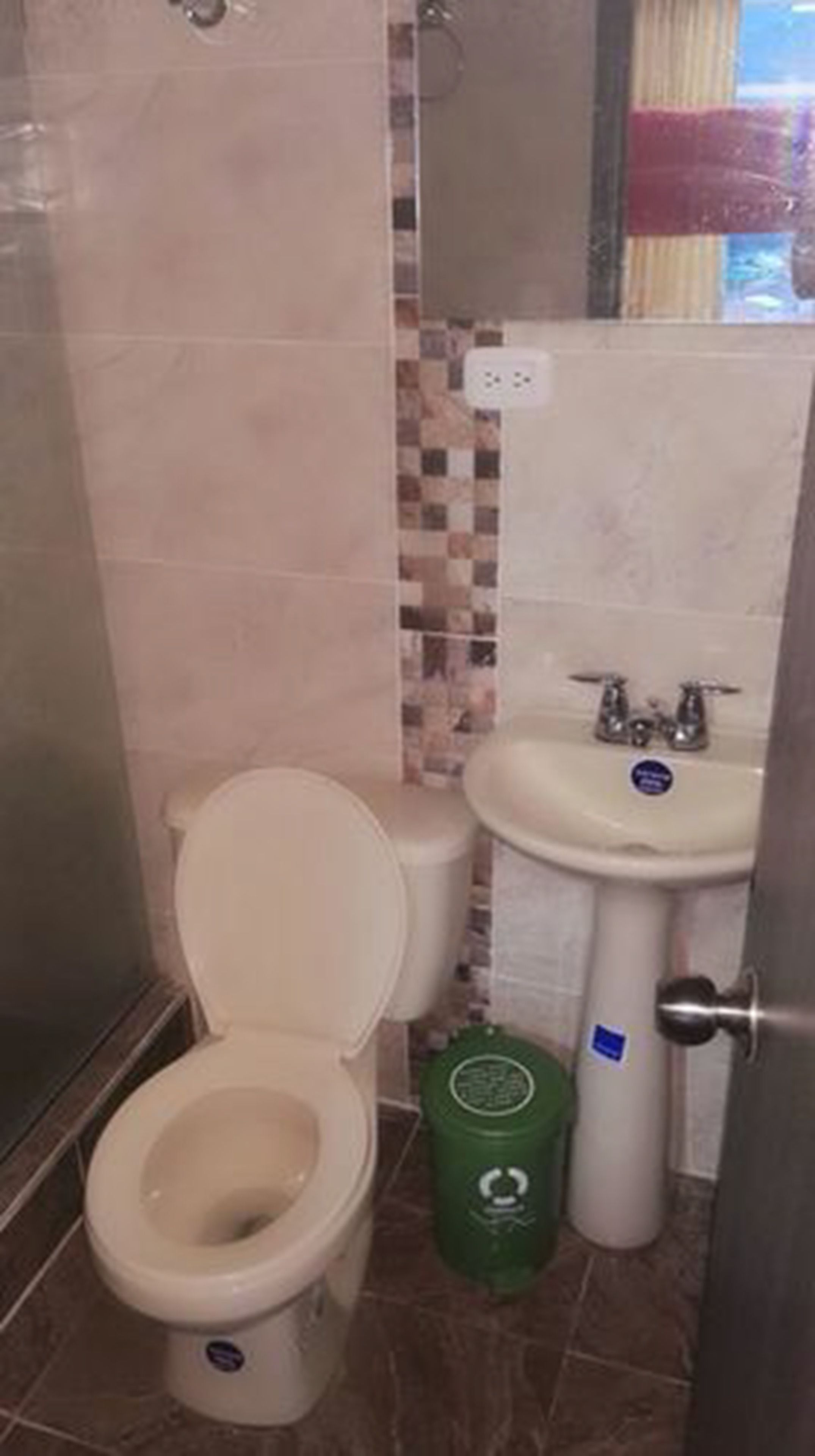 Ein Badezimmer mit Toilette, Waschbecken und einer grünen Mülltonne.
