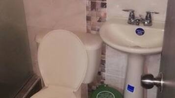 Ein Badezimmer mit Toilette, Waschbecken und einer grünen Mülltonne.