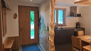A modern kitchen with a wooden accent wall, a dining area with a wooden table and chairs, and a view of the outdoors through a window. - Haus Carmen, family-friendly 4 Edelweiss holiday apartment with BergePlus program (St. Gallenkirch)