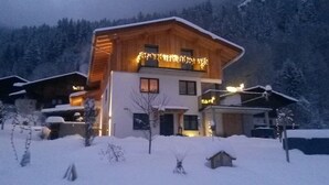 A two-story wooden cabin with a balcony, surrounded by snow-covered trees. - Haus Carmen, family-friendly 4 Edelweiss holiday apartment with BergePlus program (St. Gallenkirch)