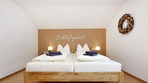 Een tweepersoonsbed met witte lakens en twee kussens, een houten hoofdbord en een wandlamp.