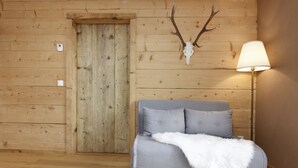 Een kamer met een houten deur, een grijze bank met een witte bontdeken en een lamp aan de rechterkant.