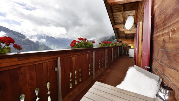 Een houten balkon met uitzicht op bergen, een witte bonttapijt en een metalen bak.