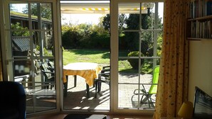 A room with a sliding glass door leading to an outdoor patio area. Inside, there is a table with chairs, a small rug, and a television on a wooden stand. - Family friendly, comfortable, cozy apartment to 5 persons (Schönberg)