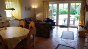 A cozy living room with a sofa, a dining table, and a chair. There is a window with curtains, a radiator, and a lamp. - Family friendly, comfortable, cozy apartment to 5 persons (Schönberg)