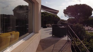 A modern outdoor area with a glass wall, outdoor furniture, and a view of trees and hills.
