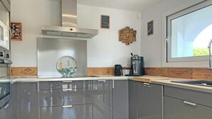 A modern kitchen with grey cabinets, a stainless steel range hood, and a window with a view of greenery.