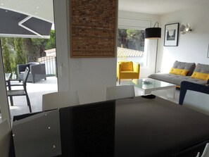 A modern living room with a glass coffee table, a sofa with yellow cushions, a yellow armchair, and a brick-patterned wall.