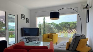 A modern living room with a sofa, chairs, a TV, and a large window with a view of trees.