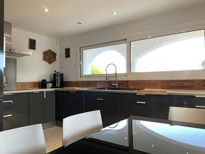 A modern kitchen with dark cabinets, a stainless steel sink, and a window with a view of greenery.