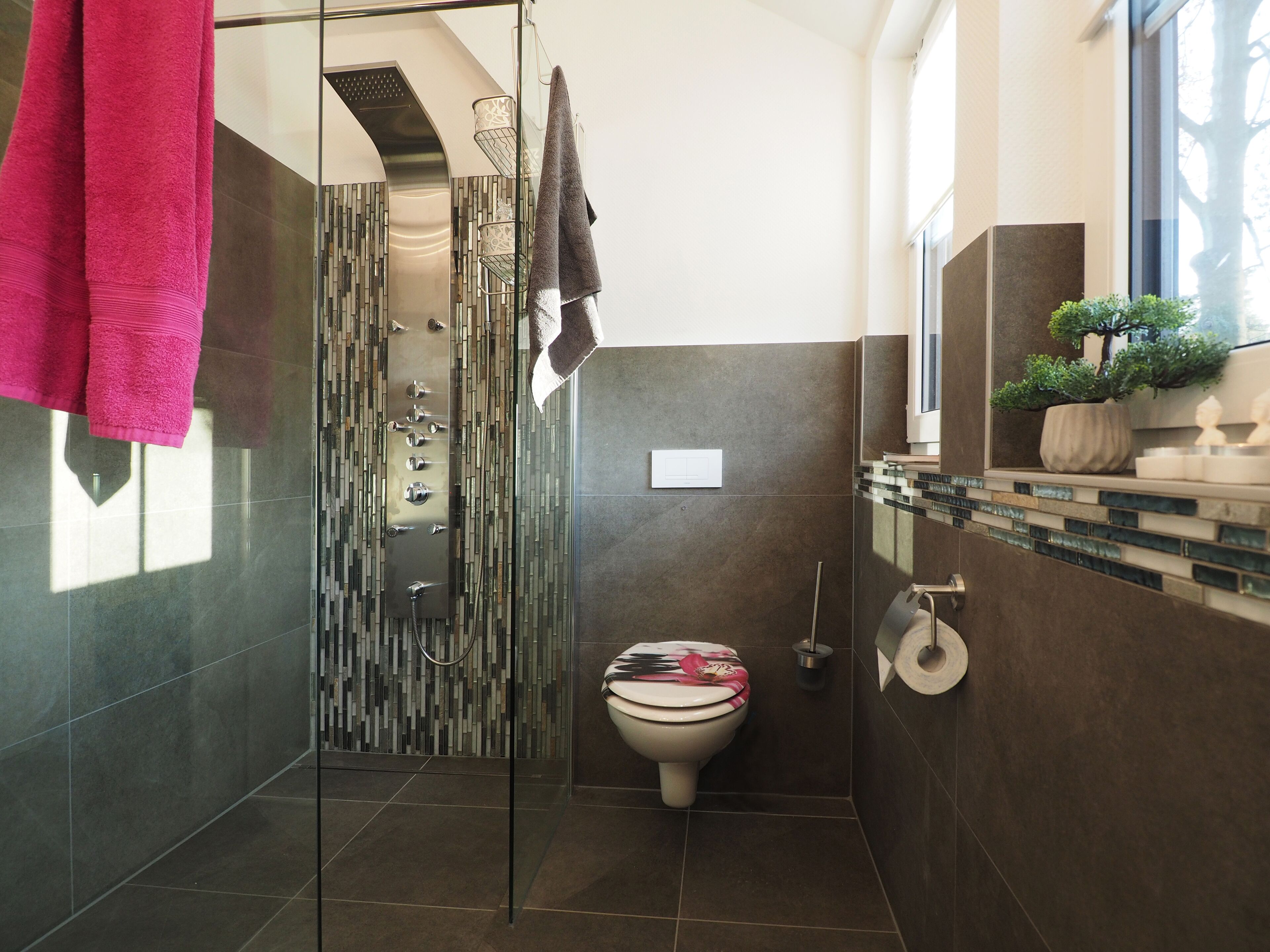 A modern bathroom with a glass shower enclosure, a toilet with a decorative cover, and a sink area with a potted plant.
