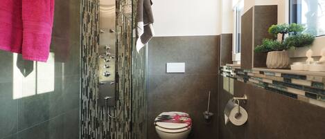 A modern bathroom with a glass shower enclosure, a toilet with a decorative cover, and a sink area with a potted plant.
