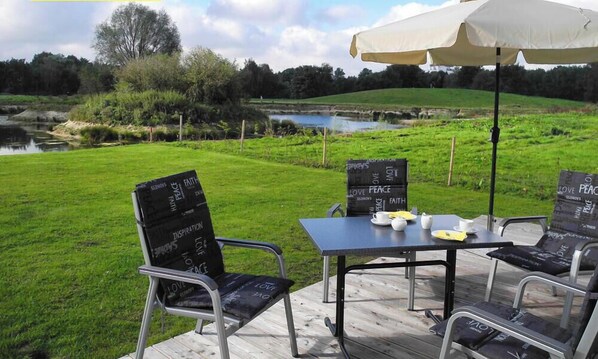 Un espace extérieur aménagé avec une table et des chaises, une terrasse en bois et une vue sur un étang et la verdure.