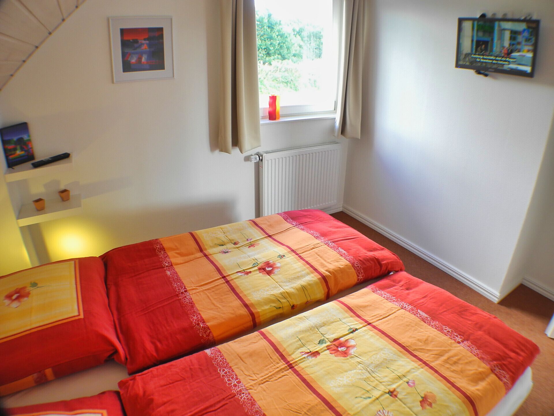 Slaapkamer met twee bedden, een raam met gordijnen, een radiator en een lijst met een afbeelding aan de muur.