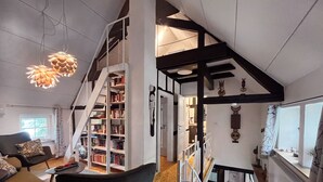 Um espaço de estar moderno em estilo loft, com escada para um andar superior, área de estar aconchegante com sofá e poltrona, e uma estante de livros bem abastecida.