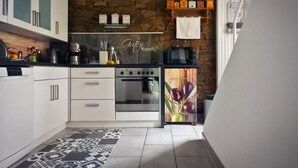Une cuisine moderne avec des armoires blanches, un four encastré, un réfrigérateur à façade décorative et un mur de pierre en guise de crédence.