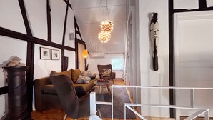 Uma sala de estar moderna com um sofá, poltronas e uma mesa de centro. Apresenta uma luminária pendente original e uma peça decorativa na parede.