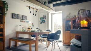 Uma área de refeições acolhedora com uma mesa de madeira, cadeiras pretas e um tapete. Há uma estante de livros e um enfeite na parede.