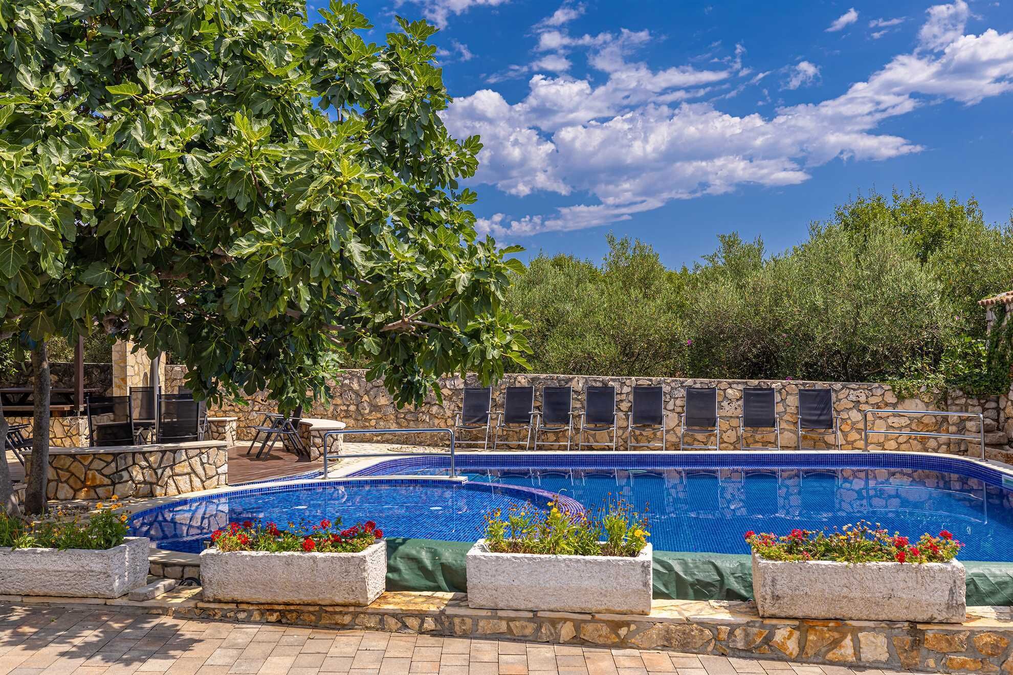 A swimming pool with stone walls and tiled edges, surrounded by planters with flowers, and outdoor seating.