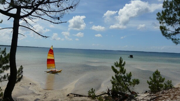 A beach with a sailboat, clear water, and a distant shoreline.