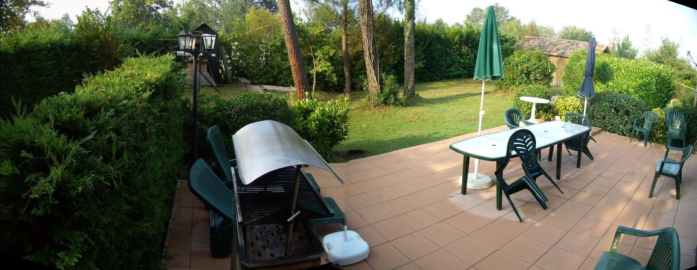 Une terrasse extérieure équipée d’un barbecue, d’une table à manger, de chaises et de parasols.