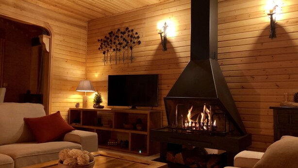 Un salon chaleureux avec une cheminée, des murs en bois, un téléviseur et des fauteuils confortables.
