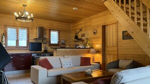 Un intérieur de chalet chaleureux, avec un revêtement mural en bois, un canapé, une table basse, un coin cuisine et un escalier.